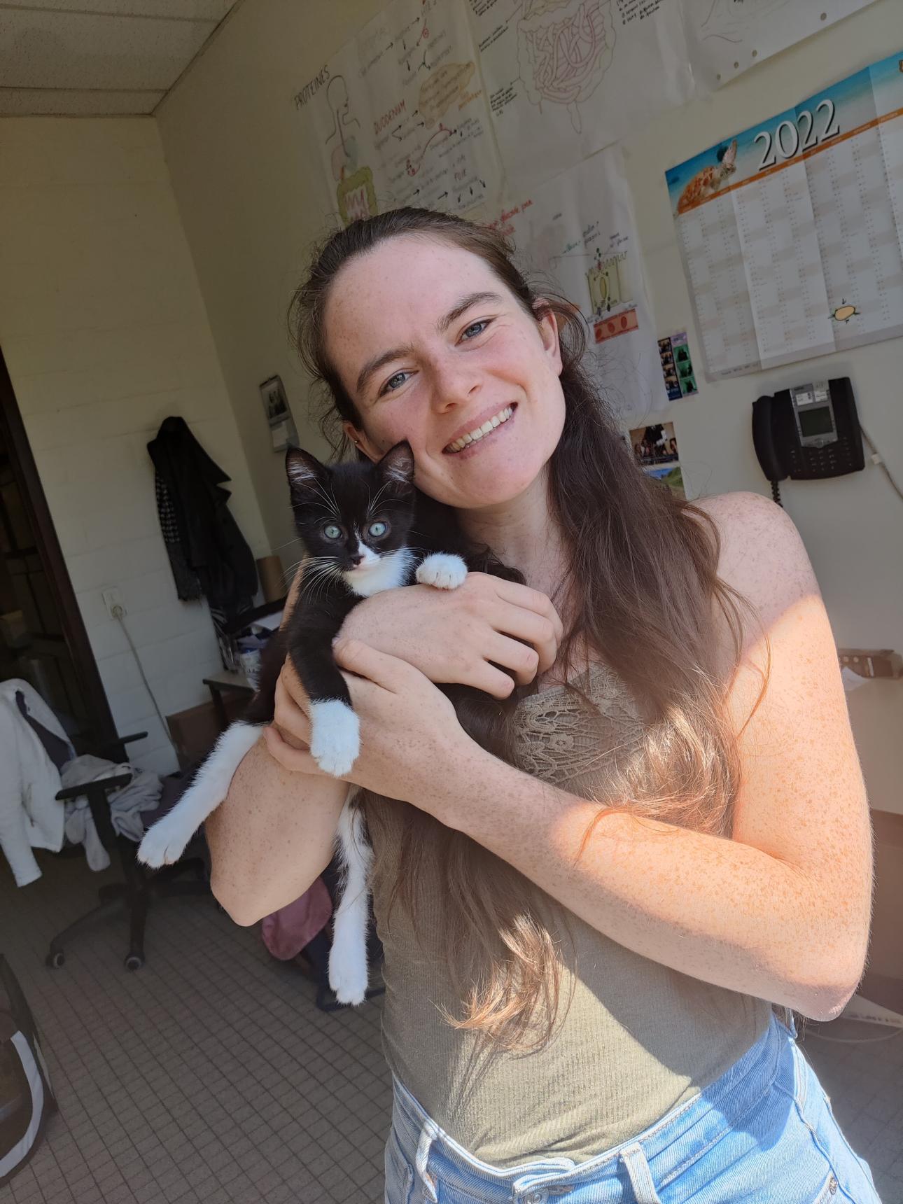 photo d'une femme avec des cheveux brun, un chaton noir et blanc dans les bras